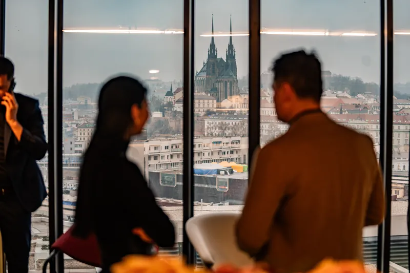 Dva lidé u prosklené stěny, v dálce katedrála svatého Petra a Pavla